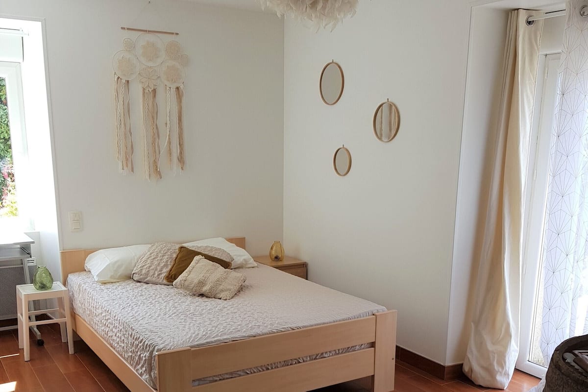 A bedroom with a wooden bed, a woven rug, and wall decorations including circular mirrors and a macrame piece.