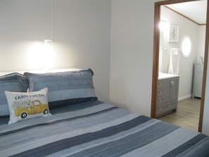 A bedroom with a bed, pillows, a dresser, and a bathroom visible through an open door.