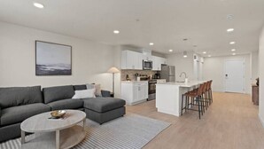 A modern apartment with a grey sectional sofa, a round coffee table, a kitchen with white cabinets, and a dining area with bar stools. - King Bed! J & K on Main Luxury Apartment 302 (Spokane)