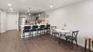 A modern kitchen with a central island, bar stools, a round dining table, and a small side table.