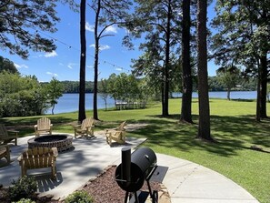 Eine Außenpatio mit Adirondack-Stühlen, einem Feuerkorb und einem Grill mit Blick auf einen See.