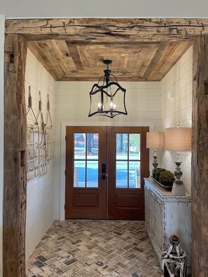 Ein Flur mit Holzboden, einem Chandelier, einer Doppeltür und einer Lampe auf einer Konsole.