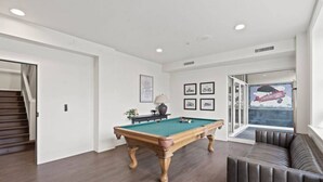 Una sala de estar moderna con mesa de billar, un sofá y una escalera que lleva a otra habitación.