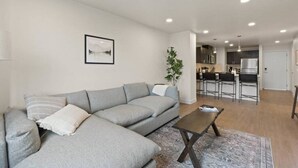 Ein modernes Wohnzimmer mit einer grauen Eckcouch, einem Couchtisch und einer Küche im Hintergrund.
