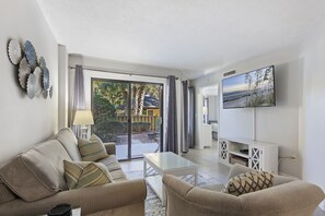 Ein Wohnzimmer mit einer Couch, Couchtisch und Fernseher. Eine Glastür führt in einen Außenbereich.