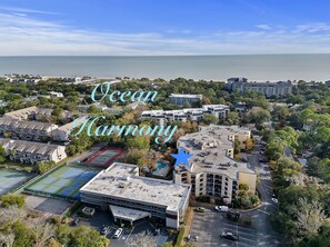 Ilmakuva Ocean Harmony -rakennuksesta, jossa näkyy suuri, useita kerroksia sisältävä rakennus, parkkipaikka ja tenniskenttä.