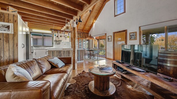 A spacious living room with a leather sofa, a wooden coffee table, and a television. - Aarlaur 2 - Charming 2BR Rustic Home l Bath l Fire Pit l WiFi Air-Con (Jindabyne)