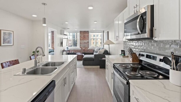 Une cuisine moderne avec des meubles blancs, une cuisinière encastrée et un four à micro-ondes. On y trouve également un coin repas avec un canapé et une lampe.