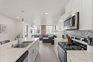 A modern kitchen with white cabinetry, a built-in stove, and a microwave. There is a dining area with a sofa and a lamp. - J & K on Main Luxury Apartment 305 (Spokane)