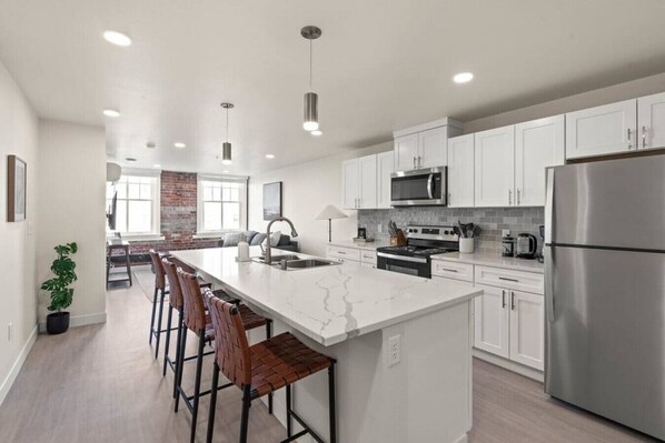 Una cocina moderna con armarios blancos, electrodomésticos de acero inoxidable y una isla central con taburetes de bar.