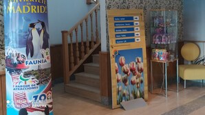 Un vestíbulo de hotel con una escalera de madera, un cartel con servicios y una vitrina de vidrio.