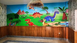 Una habitación con un mural de dinosaurios en la pared, paneles de madera en la mitad inferior y una cesta colgante.