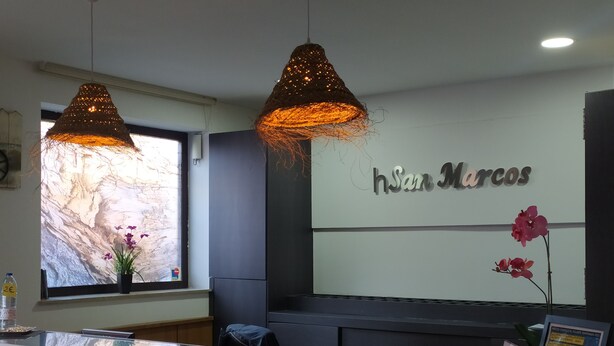 Un área de recepción de diseño moderno, con un amplio ventanal que ofrece vistas a un paisaje rocoso, dos lámparas colgantes y un mostrador de recepción con un letrero que dice "hsaam Marcos".
