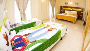 Habitación de hotel con dos camas, cada una con una colcha colorida, una cama grande con colcha amarilla, cabecero y televisor de pared.