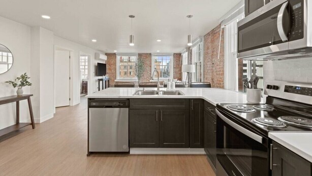A modern kitchen with a central island, stainless steel appliances, and a view of the city through large windows. - Spacious Apartment with King Beds!  J&K on Main (Spokane)