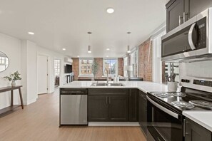 A modern kitchen with a central island, stainless steel appliances, and a view of the city through large windows. - Spacious Apartment with King Beds!  J&K on Main (Spokane)