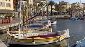 Un port de plaisance où sont amarrés plusieurs bateaux aux couleurs vives, un bâtiment imposant avec une tour en arrière-plan et un ciel dégagé.