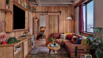 A cozy living room with wooden walls, a large window, a sofa, and a coffee table.