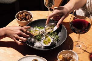 Una mesa de comedor con una fuente de ostras, un tazón de nueces y una copa de vino tinto.