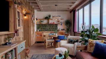 Un salon chaleureux, doté de meubles en bois, d’un coin repas et offrant une vue sur la ville grâce à de grandes fenêtres.