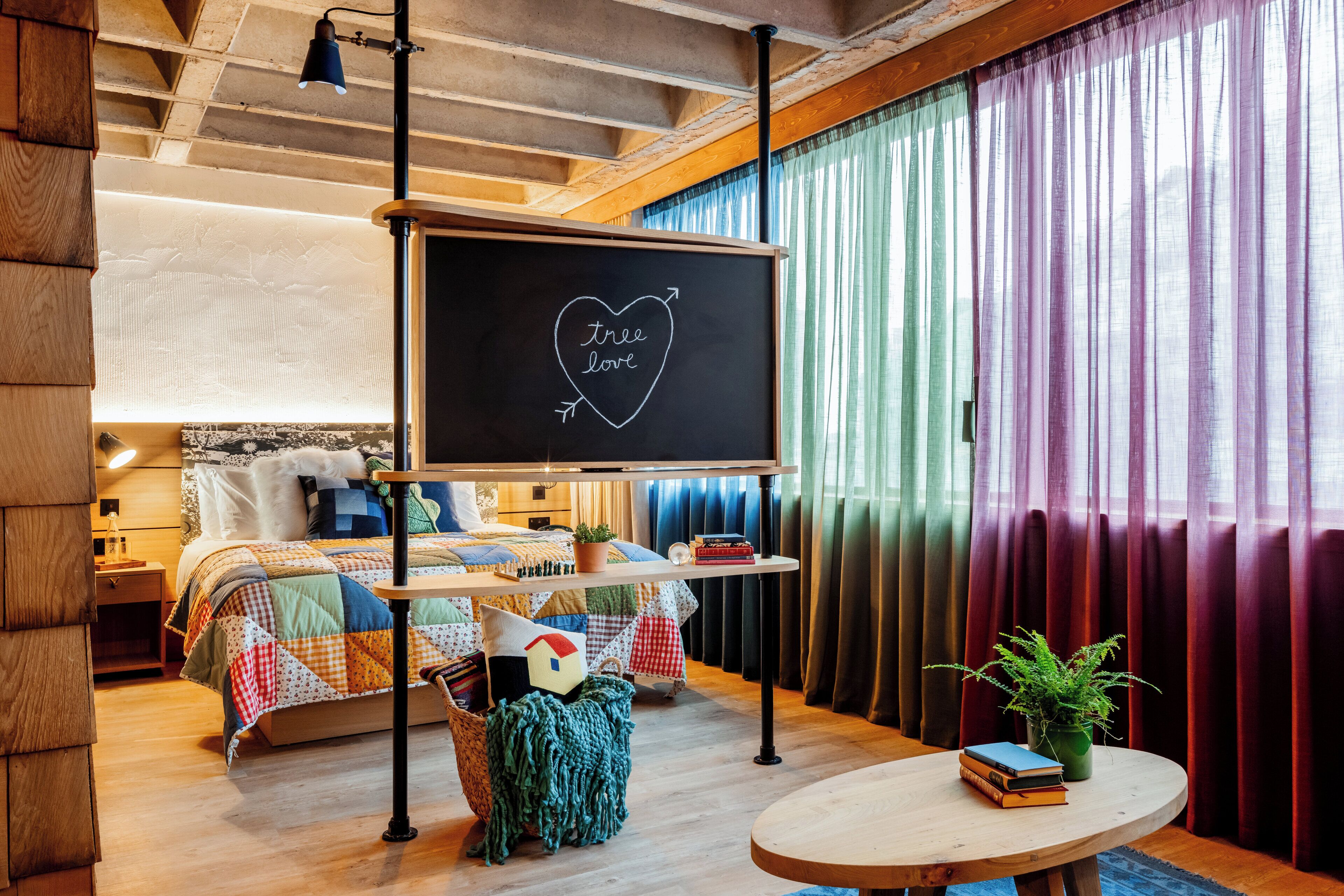 A cozy room with a bed, a round table with books, a potted plant, and a chalkboard with 'tree love' written on it.