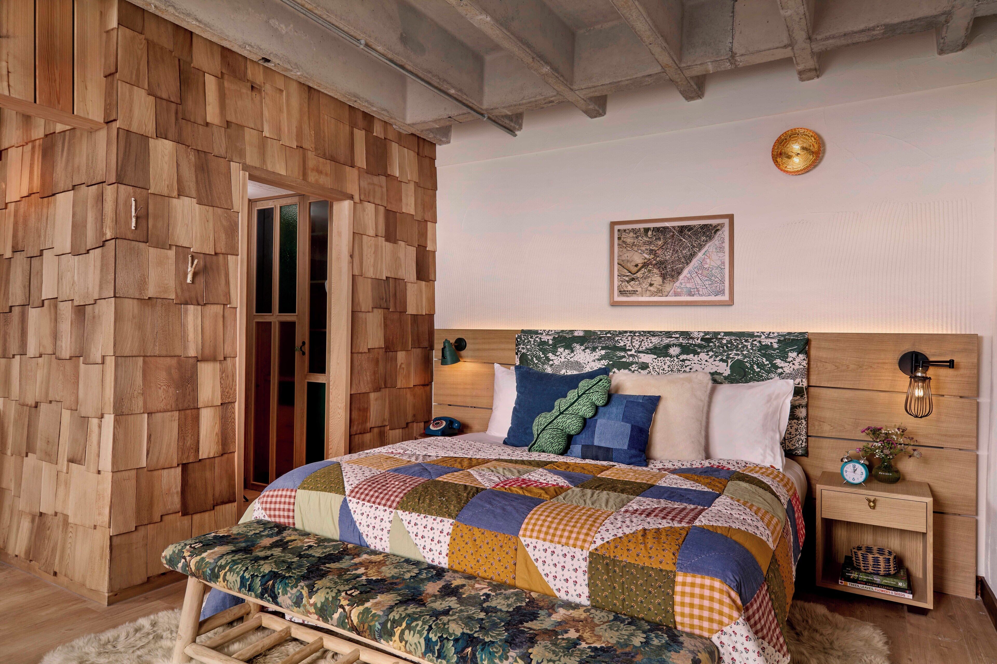 A bedroom with a wooden headboard, a quilted bedspread, and a nightstand with a lamp.