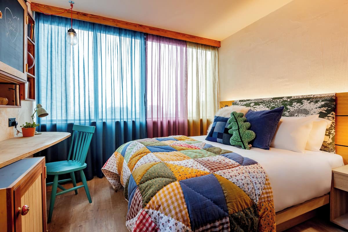A hotel room with a bed, a desk, a chair, and a window with curtains.