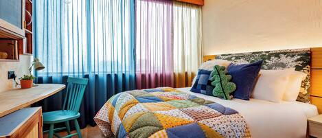 Una habitación de hotel con cama, escritorio, silla y ventana con cortinas.