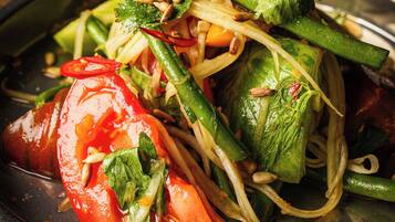 A plate of stir-fried vegetables with a variety of greens, tomatoes, and possibly some nuts.