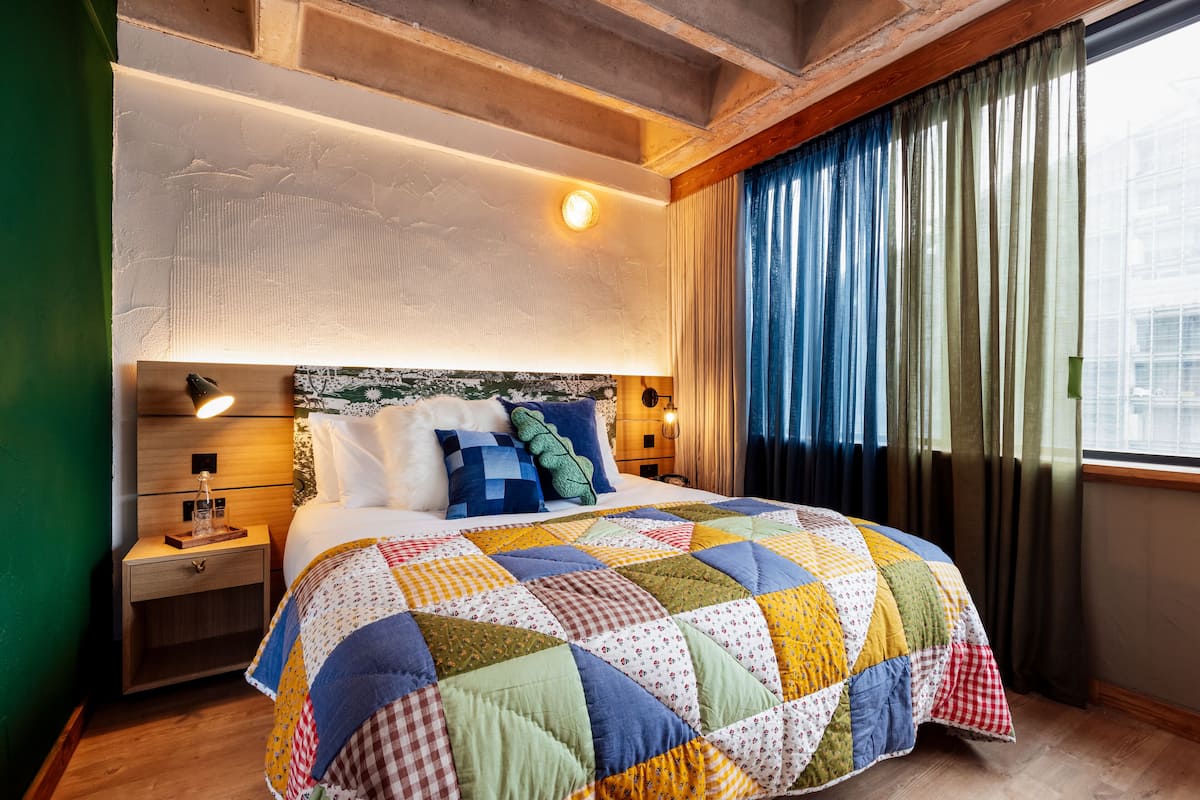 A neatly made bed with a colorful quilt, a bedside lamp, and a nightstand with a glass bottle.