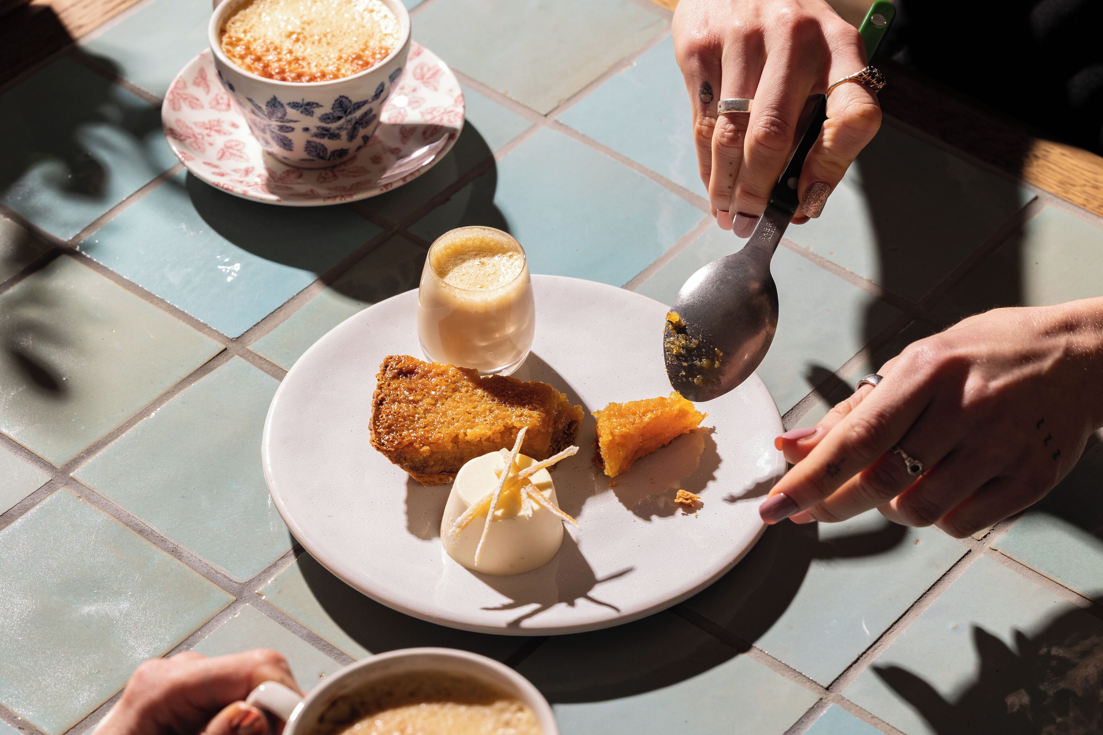 A dining table with a plate of food, a cup of coffee, and a spoon.