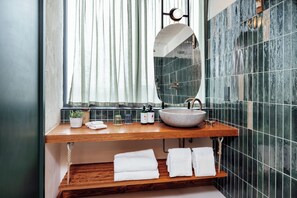 A bathroom with a wooden vanity, a round mirror, a sink, and a window with curtains.