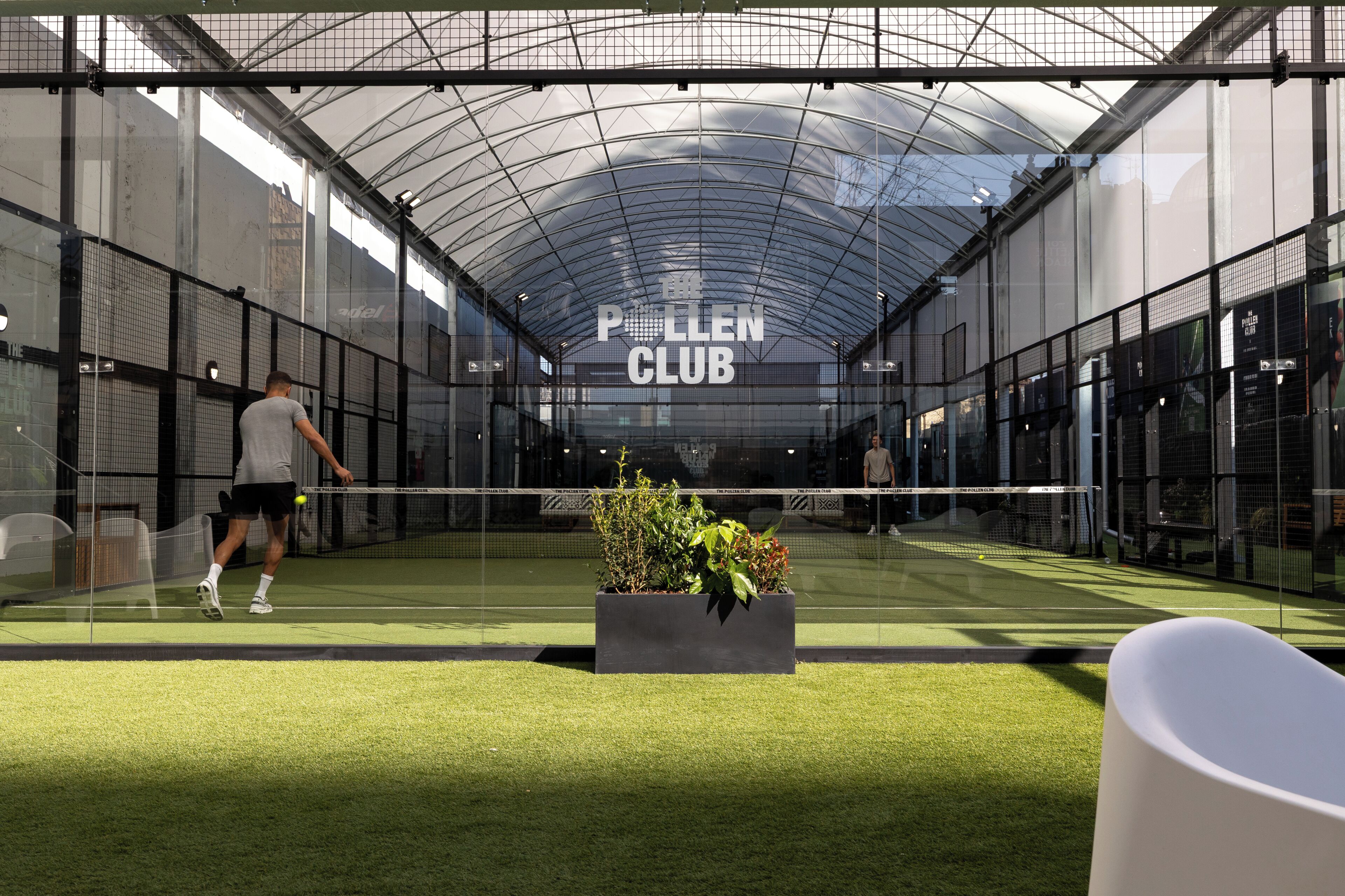 Una cancha de tenis con una red, un jugador y un letrero que dice 'Pollen Club'.