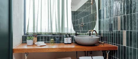 A modern bathroom with a wooden vanity, a round mirror, and a large window with sheer curtains.