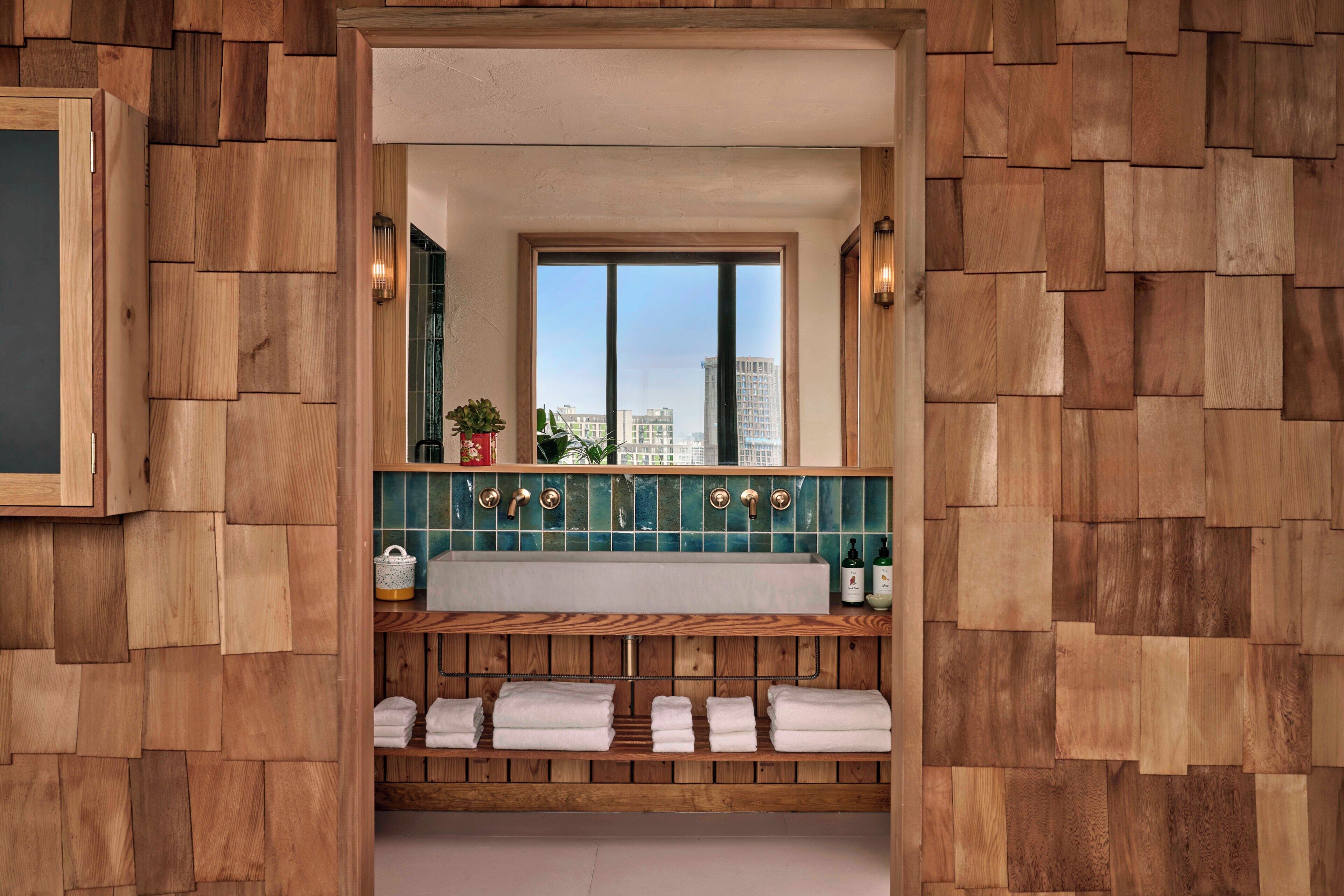 Un baño con diseño de pared de madera, un espejo grande, una ventana y un lavabo con salpicadero de azulejos.