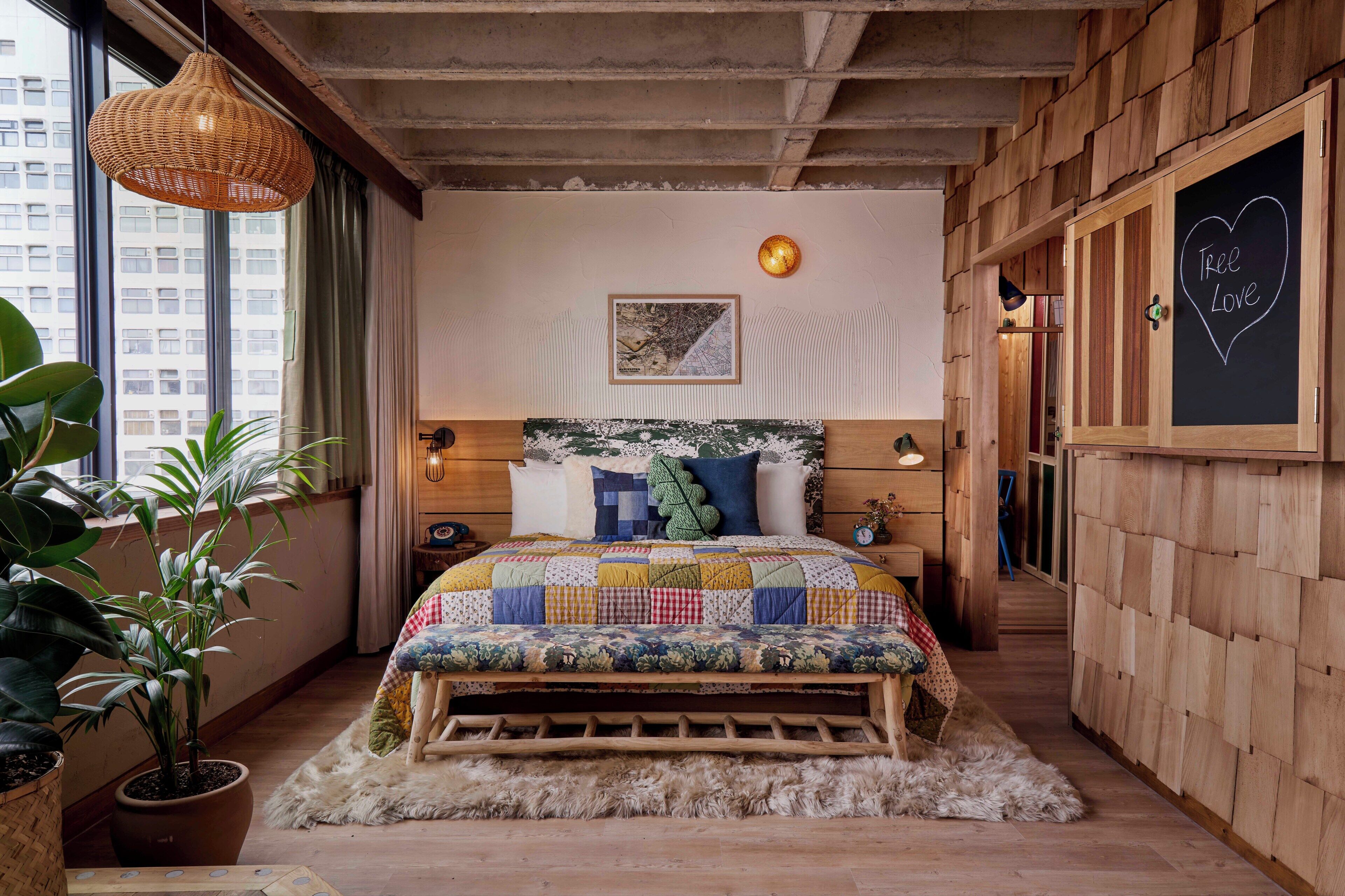 Ein Schlafzimmer mit einem hölzernen Kopfende, einer gesteppten Bettdecke, einer Karte an der Wand und einer Tafel mit dem Schriftzug 'Tree Love'.