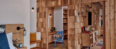 A room with a bed, a desk, and a chair, featuring wooden walls and a herringbone floor pattern.