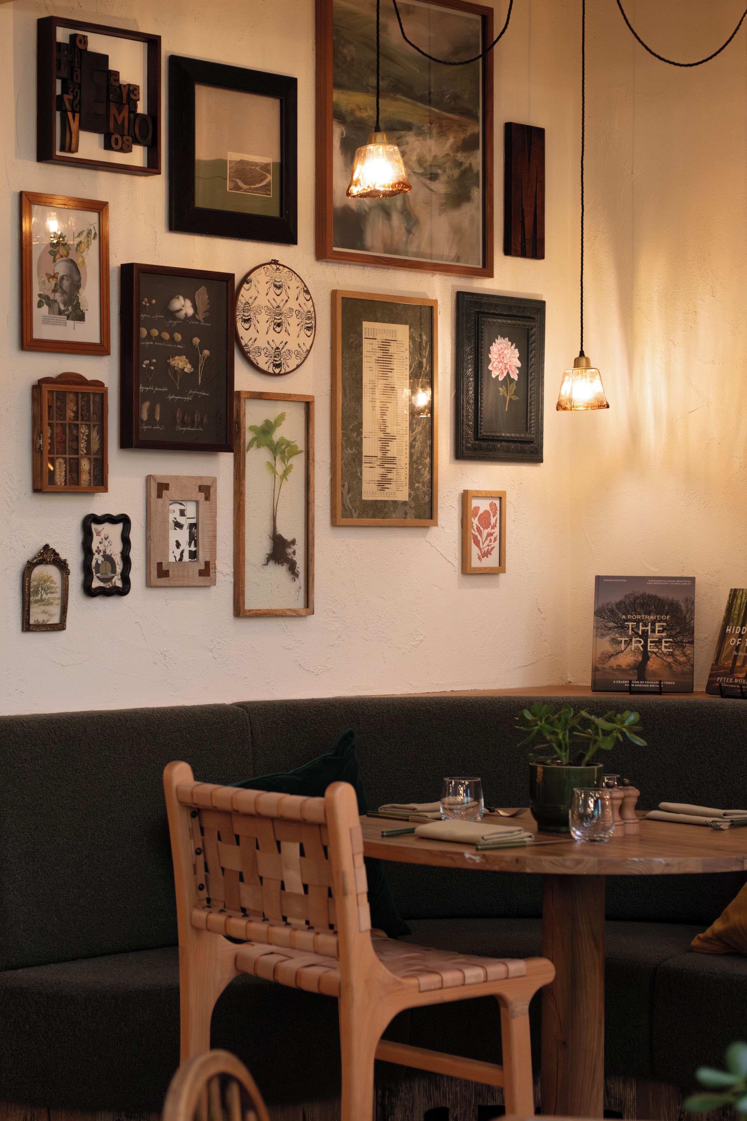 A cozy seating area with a wooden table and chairs, surrounded by various framed artworks and a bookshelf.
