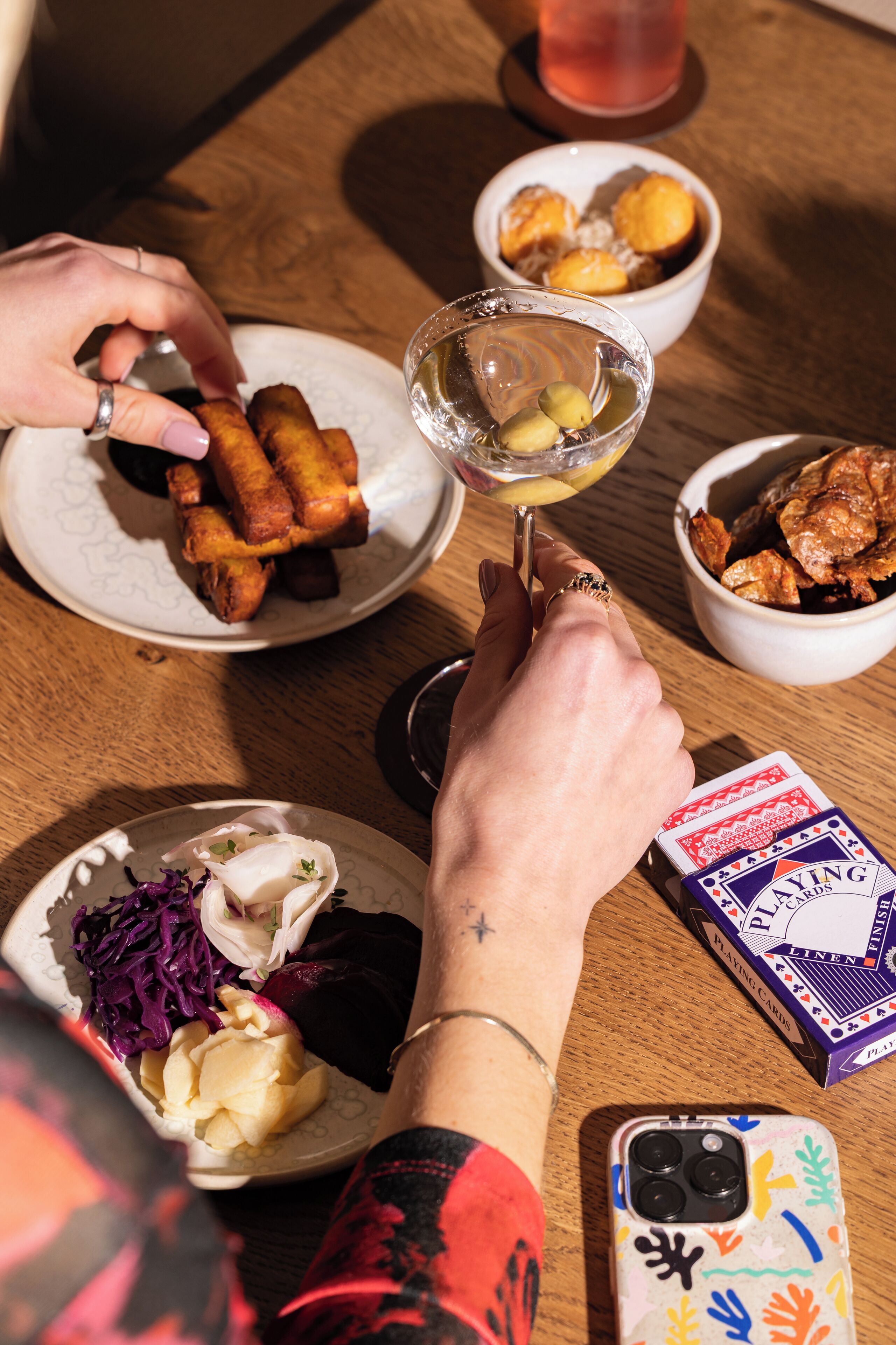 A dining table with plates of food, a glass of drink, and a deck of playing cards.