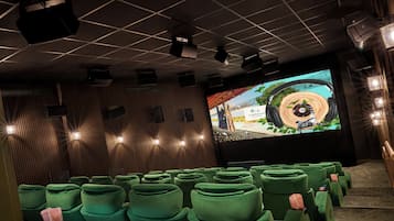 Un teatro con filas de asientos verdes, una pantalla grande y proyectores en el techo.