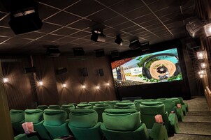 Un teatro con filas de asientos verdes, una pantalla grande y proyectores en el techo.