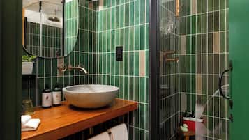 Ein Badezimmer mit einem hölzernen Waschtisch, einem großen Becken, grünen Fliesenwänden, einem Spiegel und einer Duschkabine.