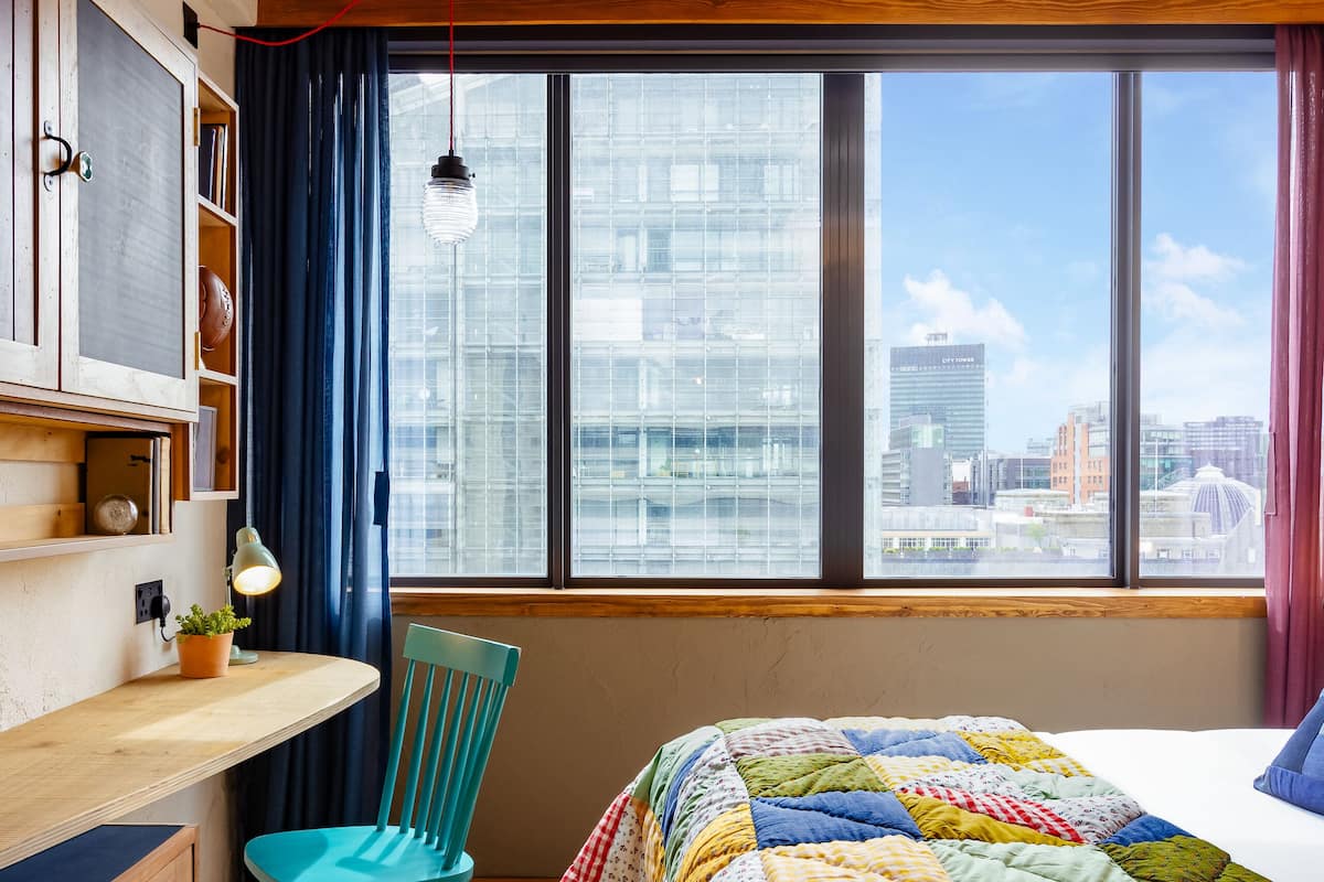 A room with a bed, a desk, a chair, and a window with a city view.
