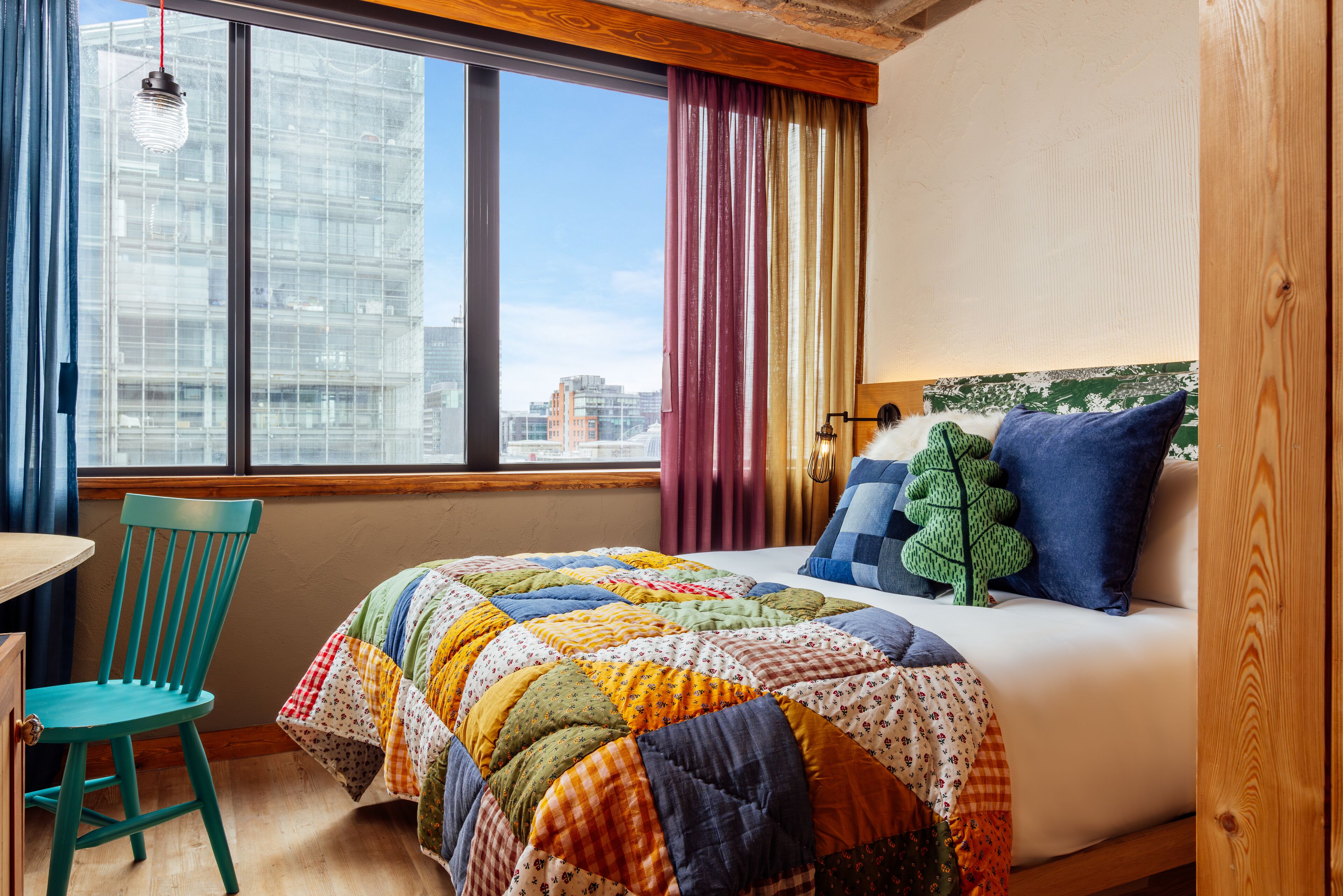 A bedroom with a large bed, a view of the city, a wooden headboard, and a window with curtains.