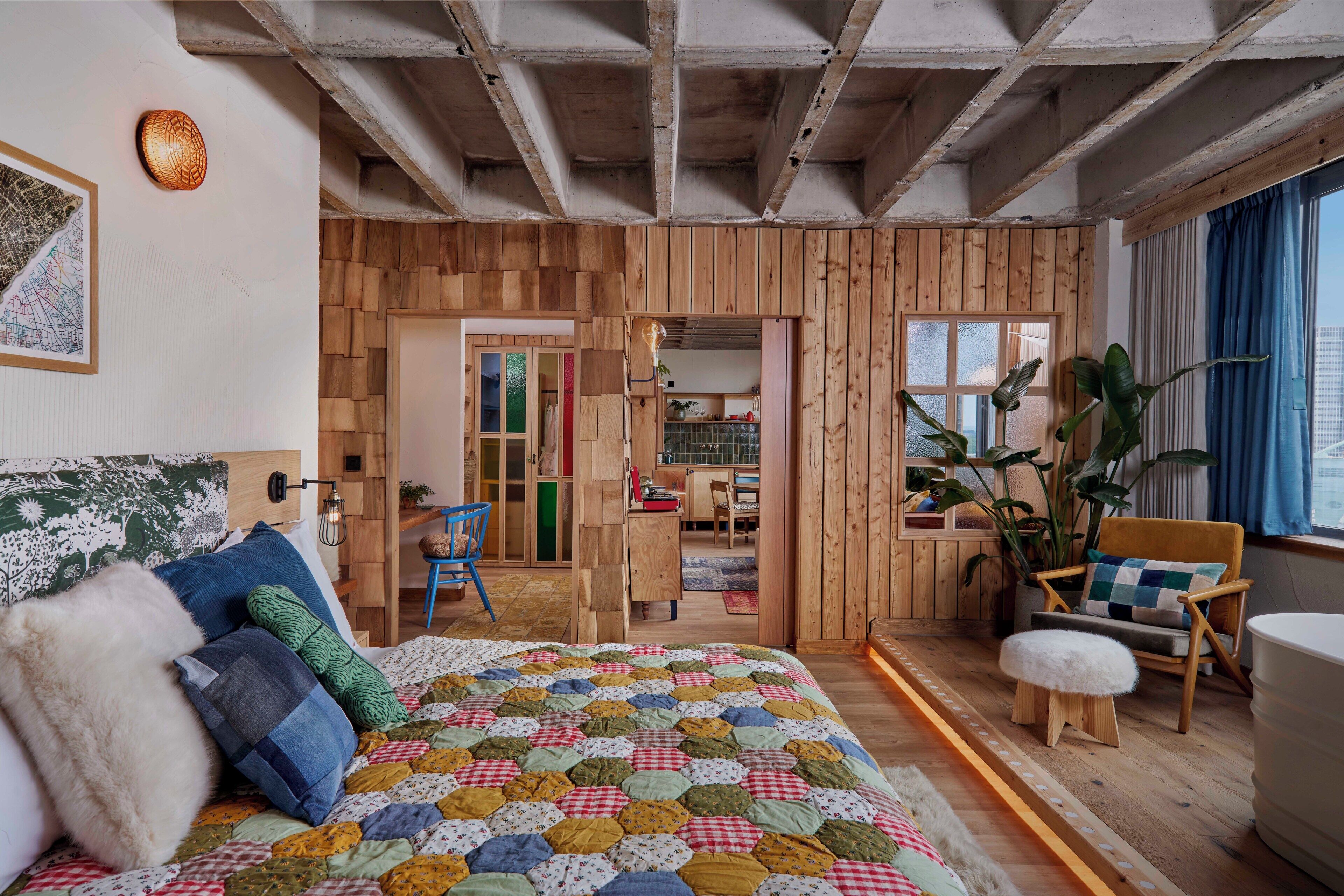 Een kamer met houten vloer, een bed met kleurrijke sprei, een houten stoel, een bureau met stoel en een raam met gordijnen.