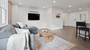 A modern living room with a grey sofa, a wooden coffee table, and a TV mounted on the wall. - King Beds! J & K on Main Luxury Apartment 406 (Spokane)