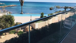 En balkon med frit udsyn til swimmingpool, palmer og havet.