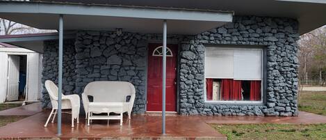 Un edificio de piedra con una puerta roja y un porche cubierto con dos sillas blancas.