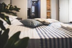 A neatly made bed with striped bedding and pillows, a plant in the foreground, and a wooden wardrobe in the background. - B&B BEL SALENTO SPECCHIA (Specchia)