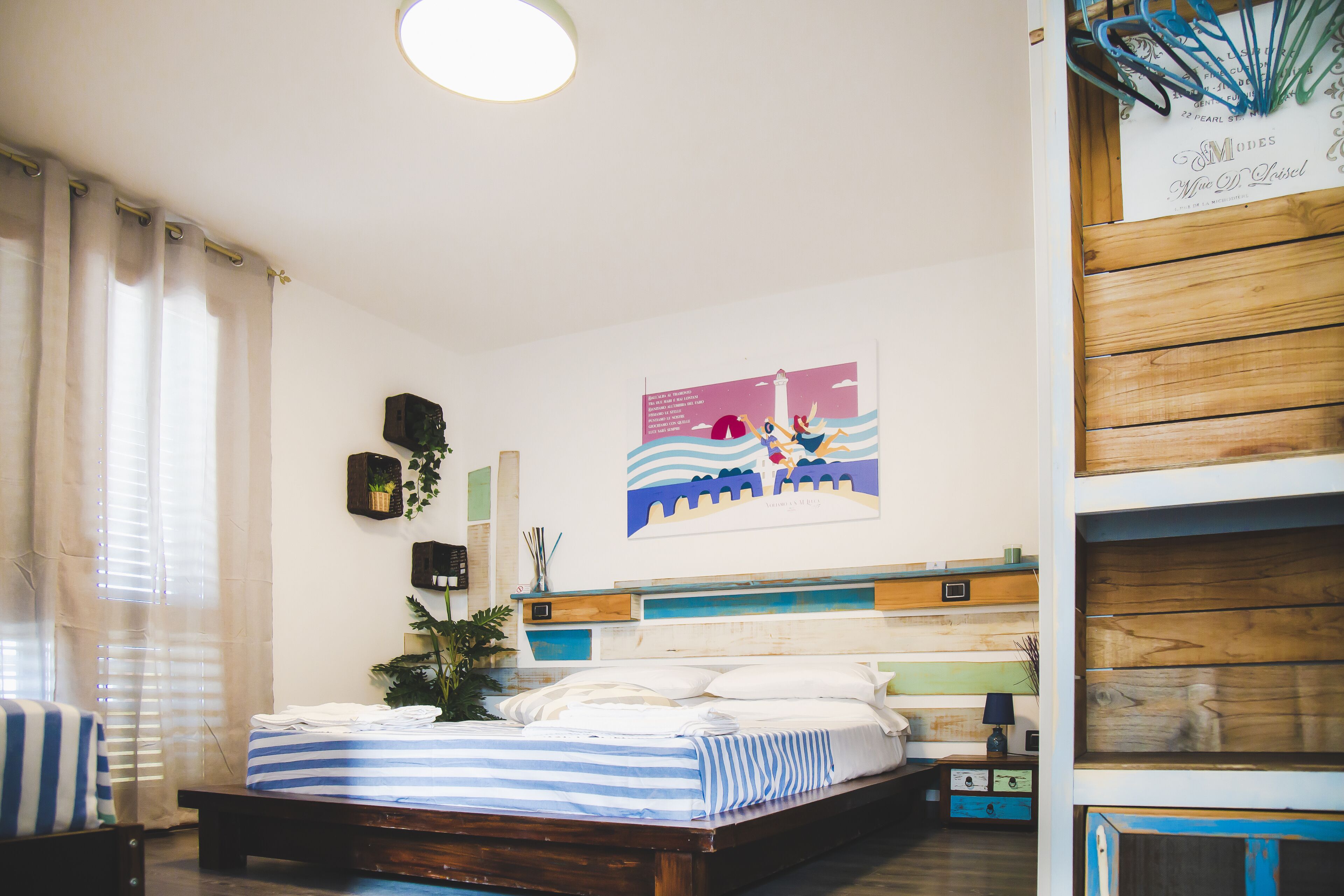 A bedroom with a bed, curtains, a wall-mounted artwork, and a wooden shelf.